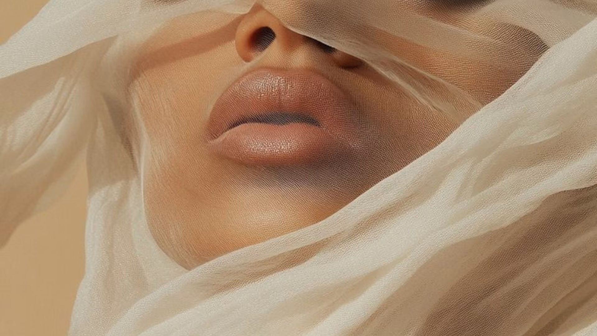 A close view of a woman's lips and chin, wrapped in folds of sheer cream fabric.